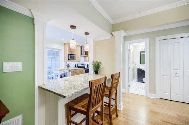 kitchen with a breakfast bar area, stainless steel appliances, light wood-style floors, ornate columns, and crown molding