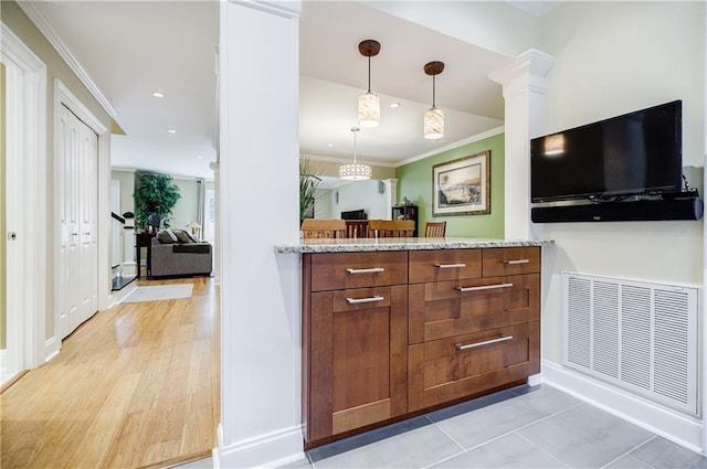 kitchen with light stone counters, visible vents, hanging light fixtures, brown cabinetry, and crown molding