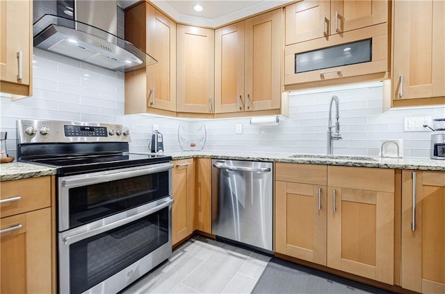 kitchen with light stone counters, stainless steel appliances, backsplash, a sink, and wall chimney range hood