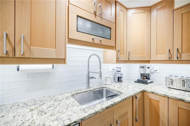 kitchen featuring light brown cabinetry, tasteful backsplash, a sink, and light stone countertops