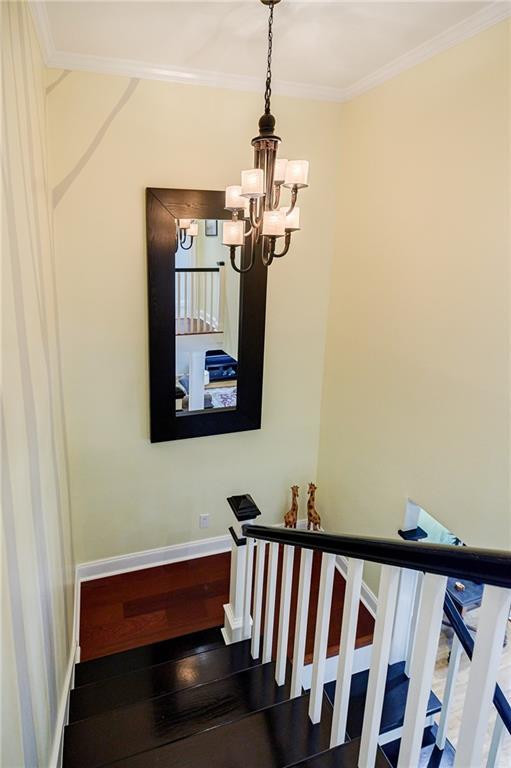 staircase featuring a chandelier, crown molding, baseboards, and wood finished floors