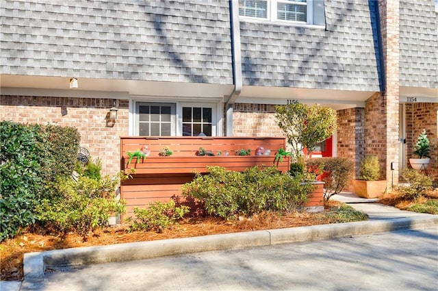 doorway to property with brick siding, mansard roof, and roof with shingles