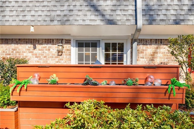 exterior details featuring brick siding, roof with shingles, a downspout, and mansard roof