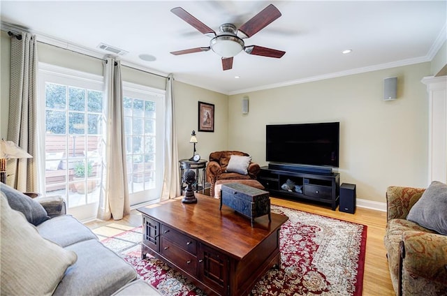 living room featuring a ceiling fan, visible vents, baseboards, ornamental molding, and light wood-type flooring