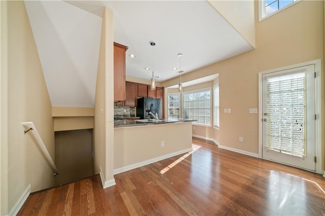 kitchen featuring decorative light fixtures, a peninsula, wood finished floors, brown cabinetry, and black fridge with ice dispenser