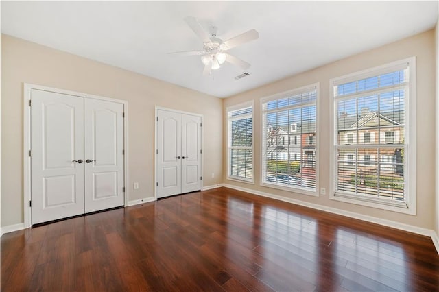 unfurnished bedroom featuring visible vents, ceiling fan, baseboards, multiple closets, and wood finished floors