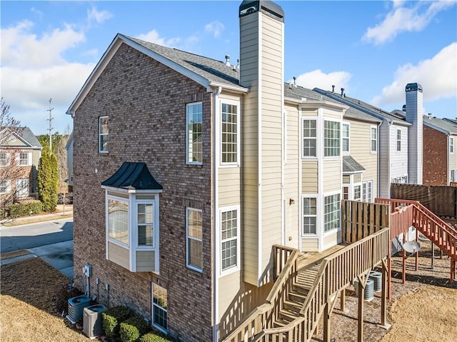 rear view of property featuring central AC unit, fence, a chimney, stairs, and brick siding