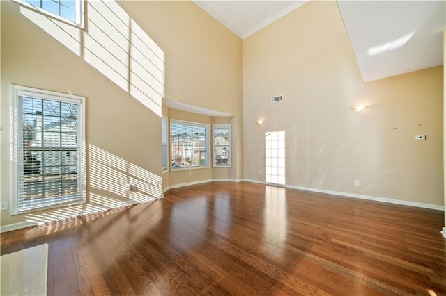 unfurnished living room with a wealth of natural light, visible vents, wood finished floors, and a towering ceiling