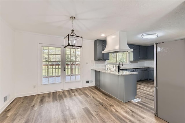 kitchen with visible vents, island range hood, decorative light fixtures, a peninsula, and backsplash