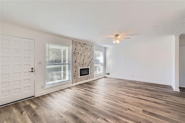 unfurnished living room featuring a large fireplace, dark wood finished floors, baseboards, and ceiling fan