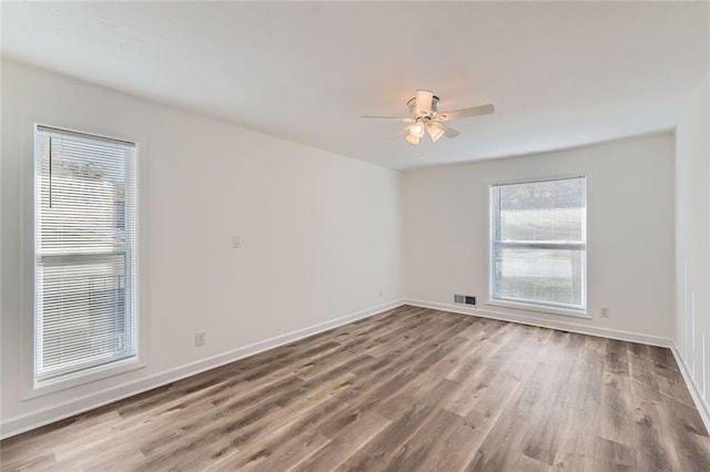 empty room featuring a healthy amount of sunlight, baseboards, and wood finished floors