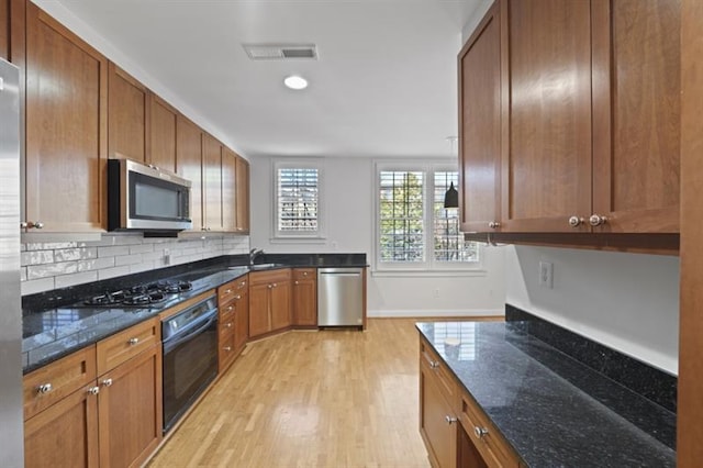 kitchen with stainless steel appliances, visible vents, decorative backsplash, dark stone countertops, and light wood-type flooring