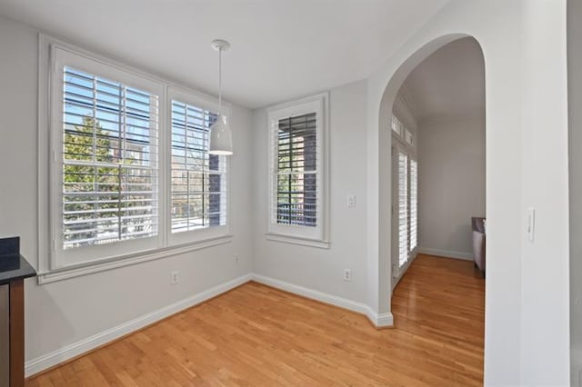 unfurnished dining area with light wood-type flooring, arched walkways, and baseboards