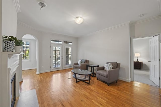 sitting room with arched walkways, a fireplace with flush hearth, baseboards, light wood-style floors, and ornamental molding