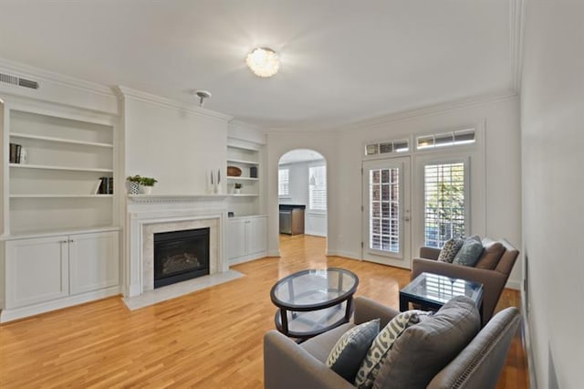 living room with visible vents, arched walkways, a fireplace with flush hearth, crown molding, and light wood-style floors