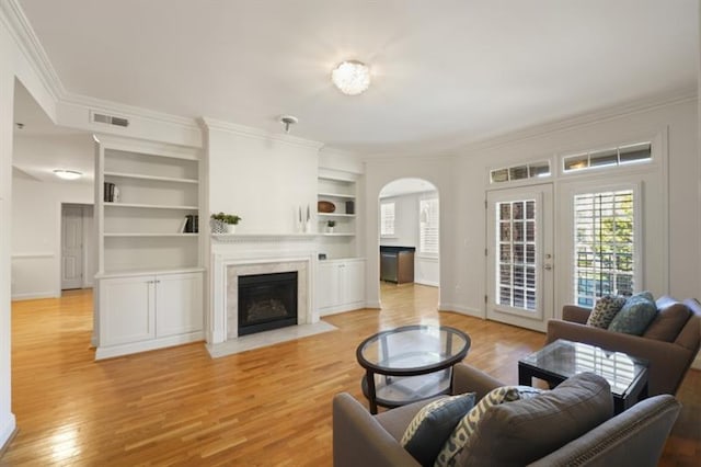 living area featuring baseboards, built in features, a fireplace with flush hearth, light wood-style flooring, and crown molding