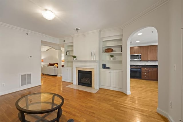 living room featuring light wood-style flooring, visible vents, a fireplace with flush hearth, and ornamental molding