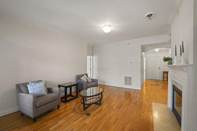 sitting room featuring light wood-style floors, baseboards, visible vents, and crown molding