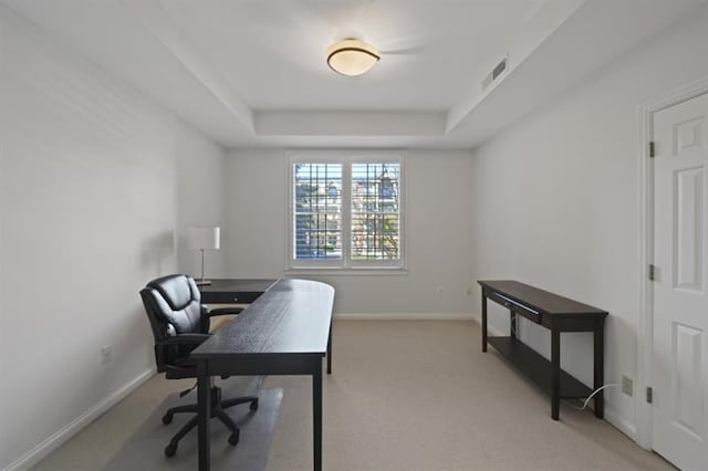 office area with baseboards, a tray ceiling, visible vents, and light colored carpet