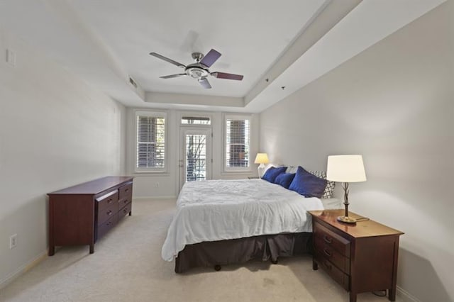 bedroom with light carpet, a tray ceiling, a ceiling fan, and baseboards