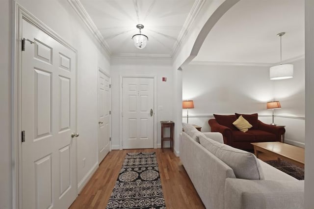 entryway with ornamental molding, arched walkways, baseboards, and light wood finished floors