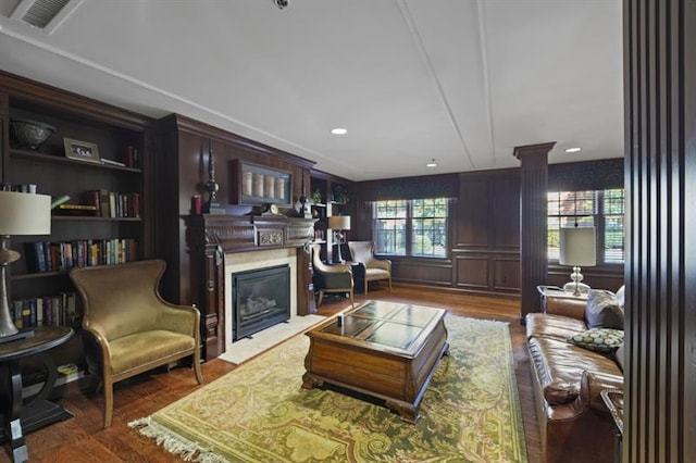 living room featuring ornate columns, a fireplace with flush hearth, visible vents, and wood finished floors