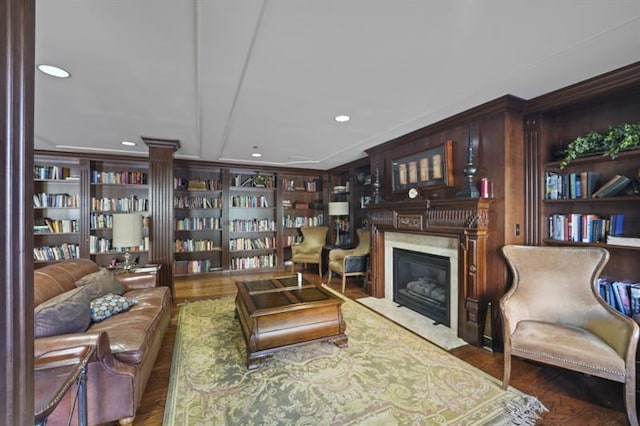 living room featuring built in shelves, a fireplace, recessed lighting, bookshelves, and wood finished floors