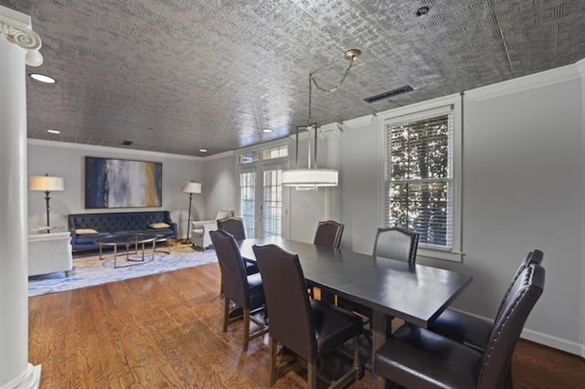 dining space with baseboards, wood finished floors, visible vents, and crown molding