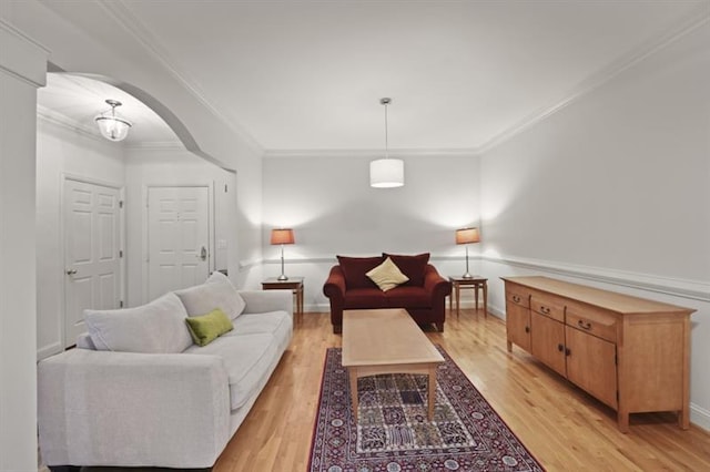 living area featuring light wood finished floors, baseboards, arched walkways, and crown molding