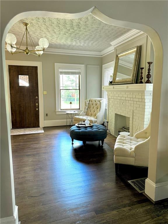 sitting room with dark wood-type flooring, a fireplace, a notable chandelier, and ornamental molding