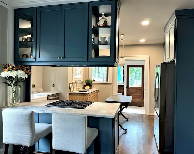 kitchen with blue cabinetry, kitchen peninsula, dark hardwood / wood-style floors, appliances with stainless steel finishes, and a breakfast bar