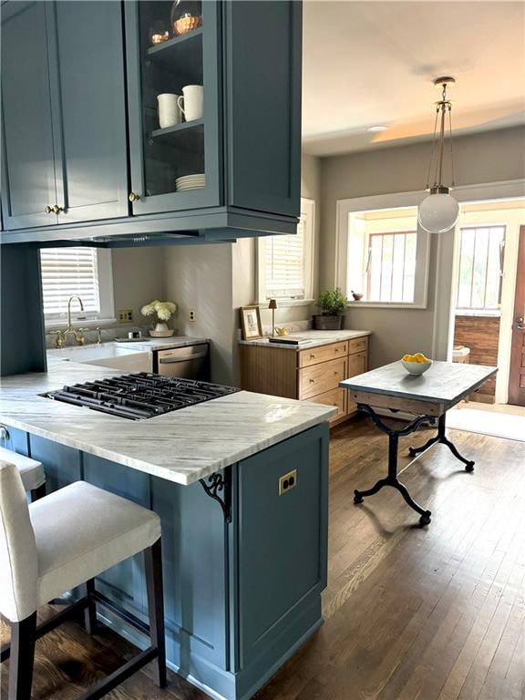 kitchen with hanging light fixtures, appliances with stainless steel finishes, kitchen peninsula, dark wood-type flooring, and a kitchen bar