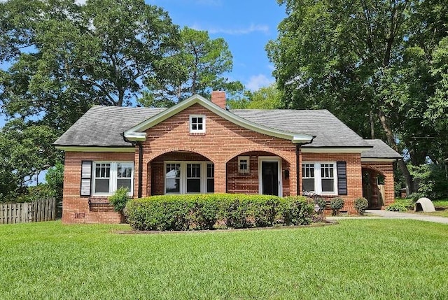 view of front of house featuring fence, a shingled roof, a chimney, a front lawn, and brick siding