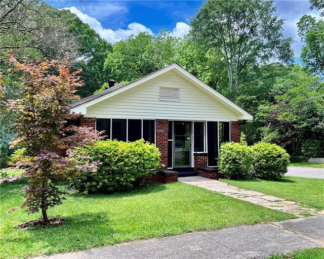 view of front of property featuring a sunroom, a front lawn, and brick siding