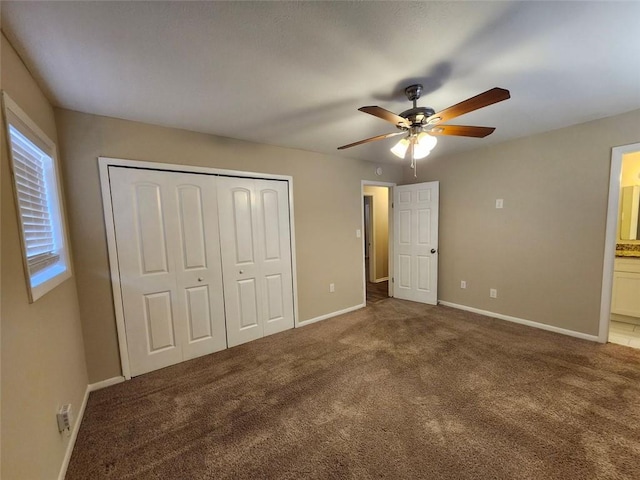 unfurnished bedroom with a closet, ceiling fan, dark carpet, and connected bathroom