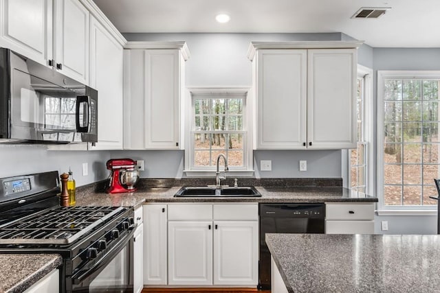 kitchen with dark countertops, black appliances, white cabinets, and a sink