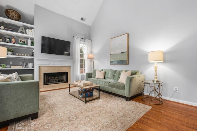 living room featuring baseboards, a fireplace with flush hearth, wood finished floors, built in shelves, and high vaulted ceiling