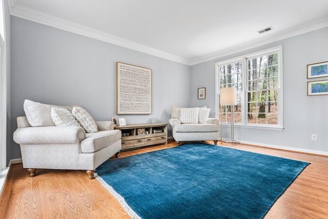 living area featuring baseboards, wood finished floors, visible vents, and crown molding