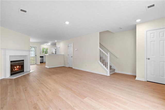 unfurnished living room with light wood finished floors, visible vents, and stairway