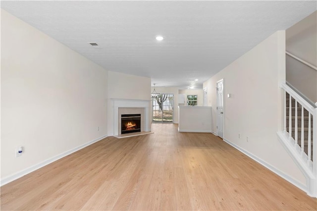 unfurnished living room with recessed lighting, light wood finished floors, a warm lit fireplace, baseboards, and stairs