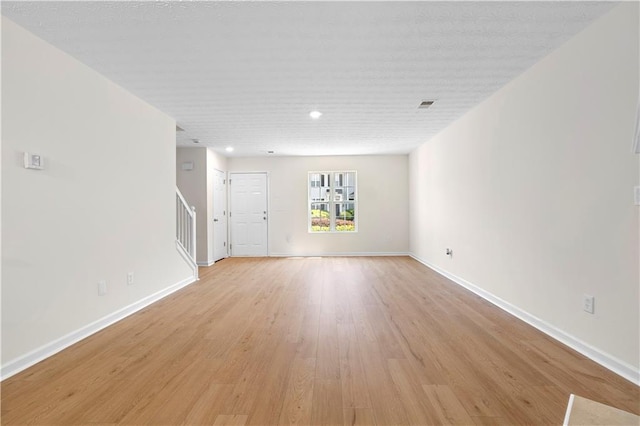 unfurnished living room featuring light wood-style floors, stairway, visible vents, and baseboards