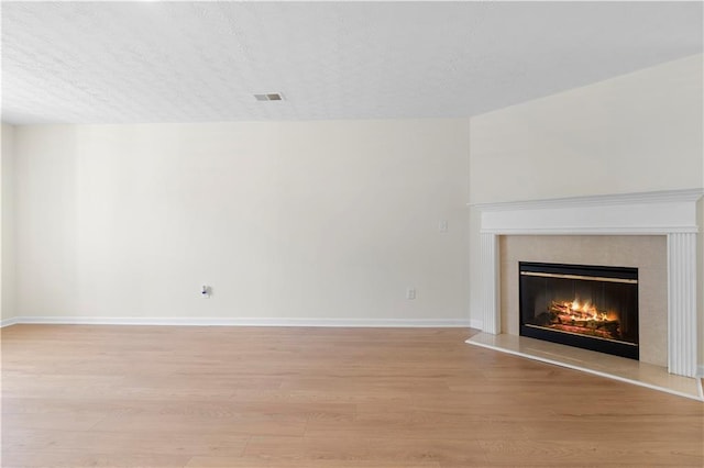unfurnished living room featuring baseboards, visible vents, light wood-type flooring, and a premium fireplace