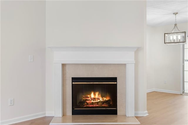 room details with a glass covered fireplace, wood finished floors, baseboards, and an inviting chandelier