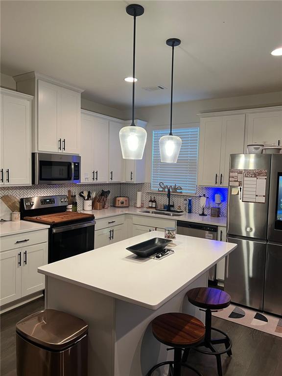 kitchen featuring hanging light fixtures, white cabinets, stainless steel appliances, and tasteful backsplash