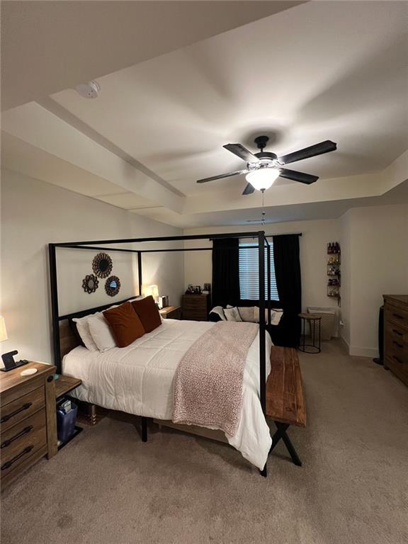 carpeted bedroom featuring ceiling fan and a raised ceiling