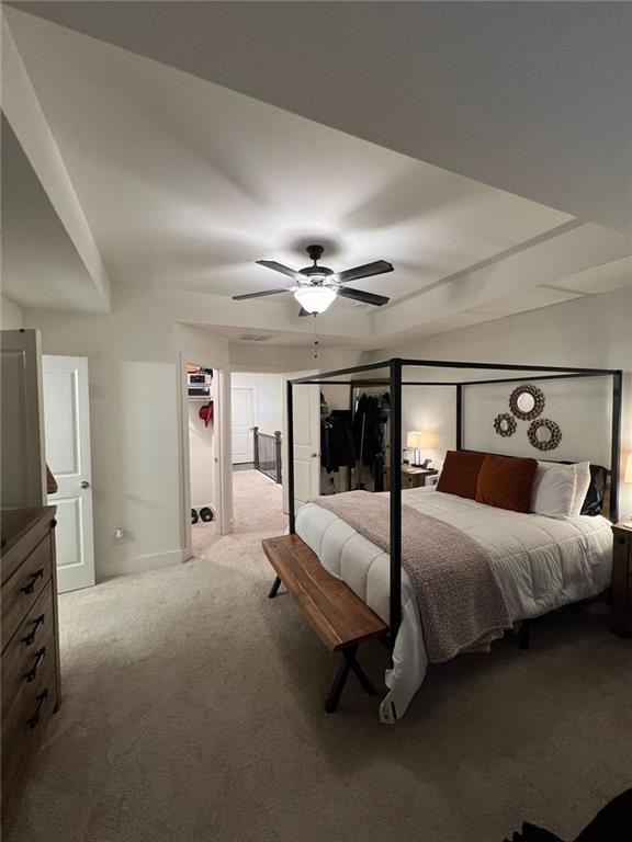 bedroom featuring ceiling fan, light colored carpet, and a tray ceiling