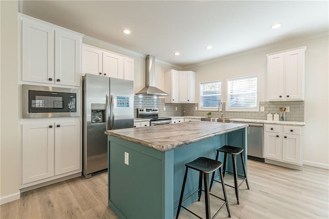 kitchen with white cabinets, light hardwood / wood-style flooring, appliances with stainless steel finishes, wall chimney range hood, and a kitchen island