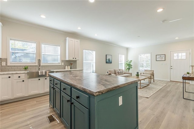 kitchen with white cabinets, light hardwood / wood-style flooring, sink, a kitchen island, and tasteful backsplash