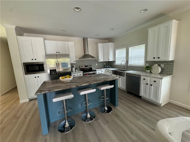 kitchen featuring stainless steel appliances, a kitchen island, a breakfast bar, white cabinets, and wall chimney range hood