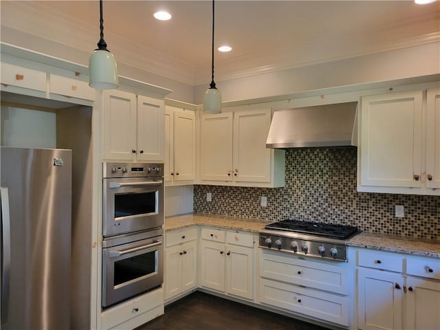 kitchen with appliances with stainless steel finishes, pendant lighting, tasteful backsplash, white cabinetry, and wall chimney exhaust hood